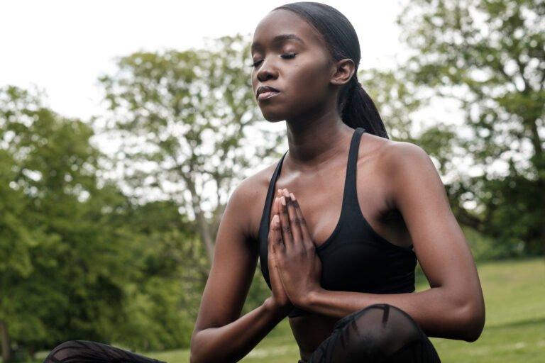 Young black woman doing meditation and yoga in a park. She is wearing black sport outfit.