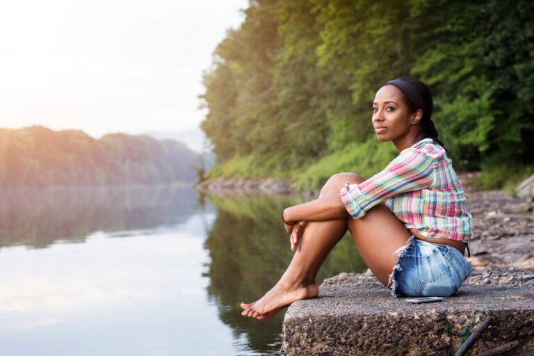 Side View Of Woman Looking Away While Sitting On Rock Against Lake In Forest